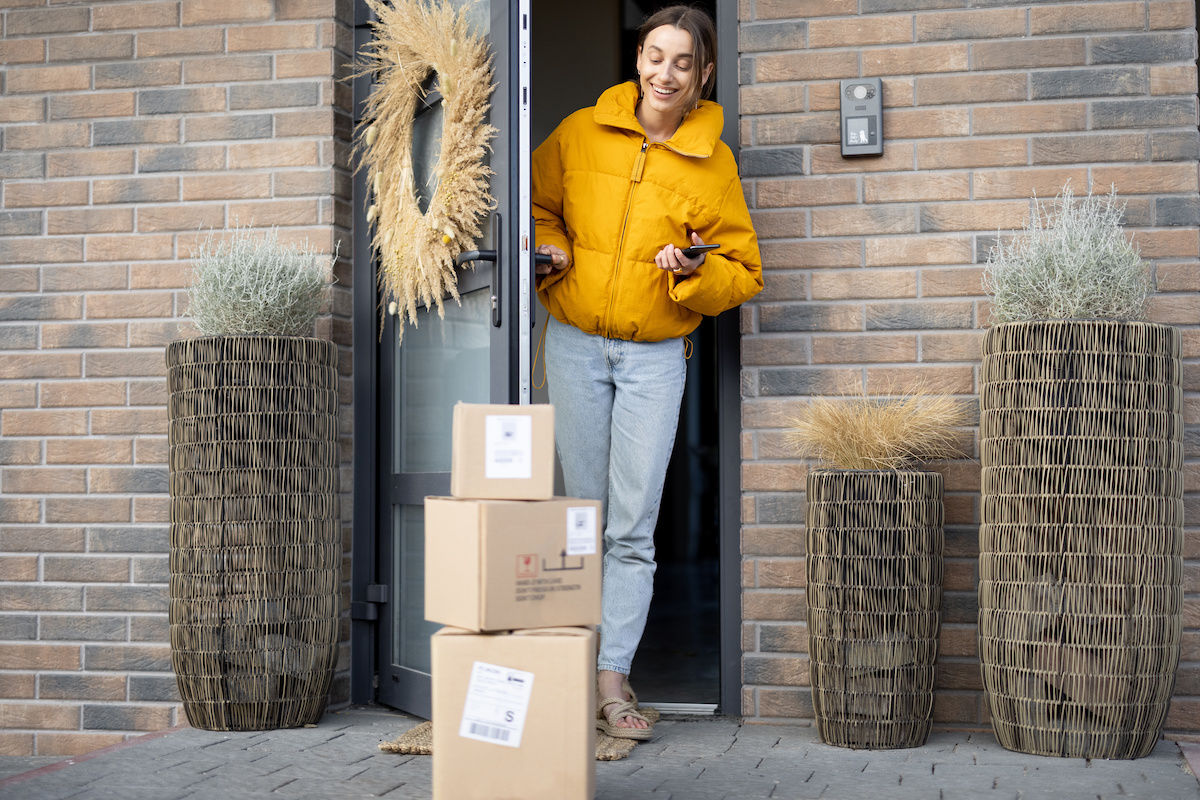 Last mile delivery logistics. A young woman in a yellow jacket picks up parcels left on the doorstep.